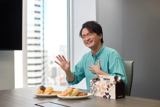 ドーナツを前に笑顔でインタビューに応じる奥村泰人さん