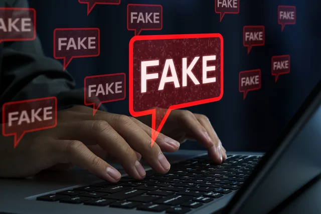 ディープフェイクや偽情報を示す「FAKE」の文字とPCを操作する手