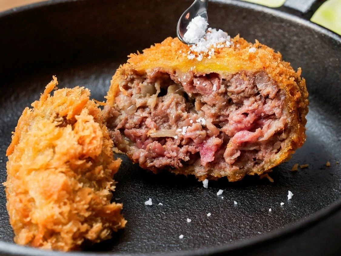 揚げたてのメンチカツに塩をかける様子