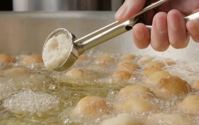 丸亀うどーなつを手づくりする様子。揚げ油の中にドーナツ生地を投入している。