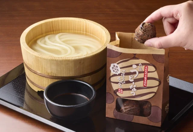 温かいうどんと「丸亀うどーなつ 濃厚ダブルチョコ ごほうびチョコ味」を一緒に楽しむ様子。