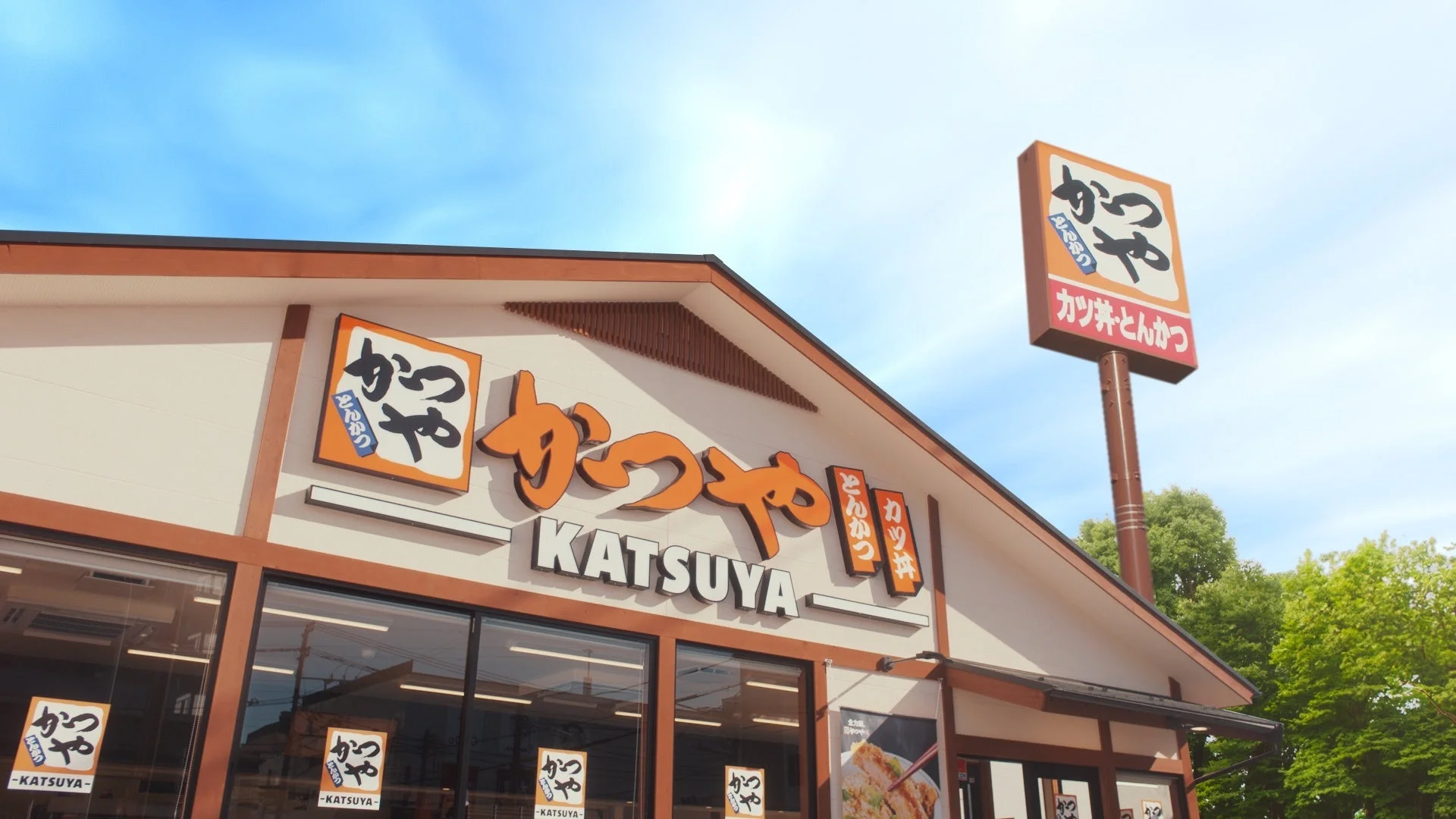 とんかつ専門店「かつや」の店舗外観。青空の下に看板が見える。