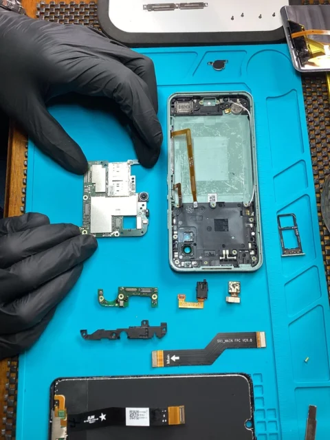 分解されたAndroidスマートフォンの基板と部品、修理作業の様子