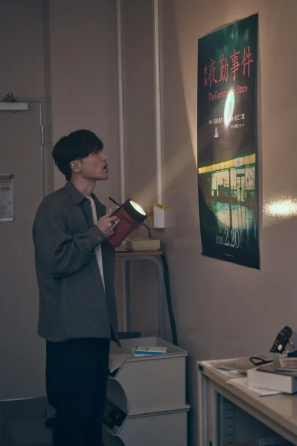 懐中電灯で「夜勤事件」のポスターを照らす鬼川治男（半田周平）