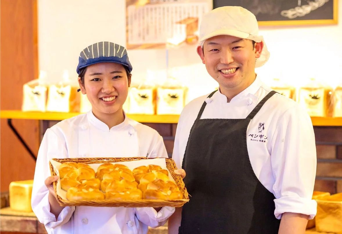 焼きたてパンを持つペンギンベーカリーのスタッフ