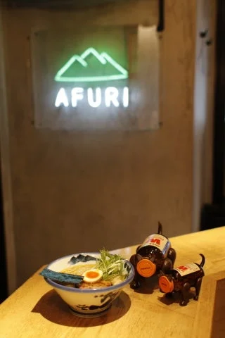 AFURIの店内を背景にラーメンと瓶犬が並ぶ