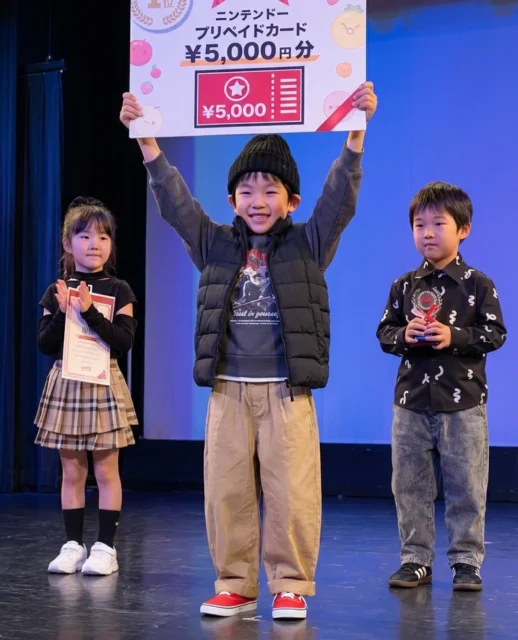 マリオカート大会でニンテンドーカードの賞品ボードを持つ子どもたち
