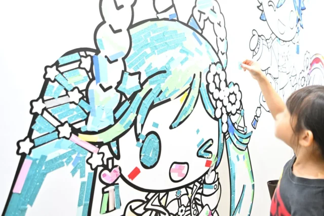 子供が初音ミクのイラストにシールを貼って楽しむ創作体験コーナー