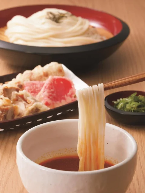 ピリ辛ごまだれつけ麺のアップ写真、箸でうどんを濃厚ごまだれにつけている