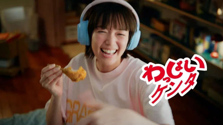 ヘッドホンをしてチキンにかぶりつき笑顔を見せる佐藤栞里さん