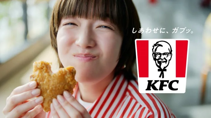 チキンを手に笑顔の佐藤栞里さんと新タグライン「しあわせに、ガブッ。」KFCロゴ