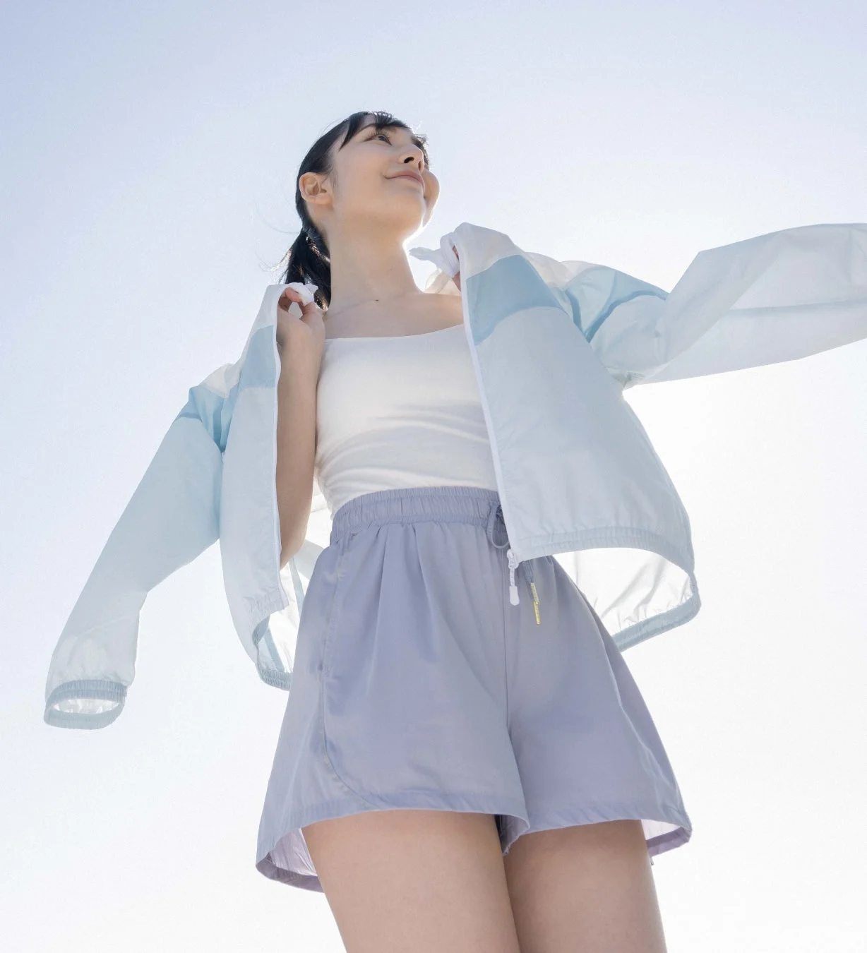 青い軽量はっ水パーカーを羽織り、空を見上げる女性。