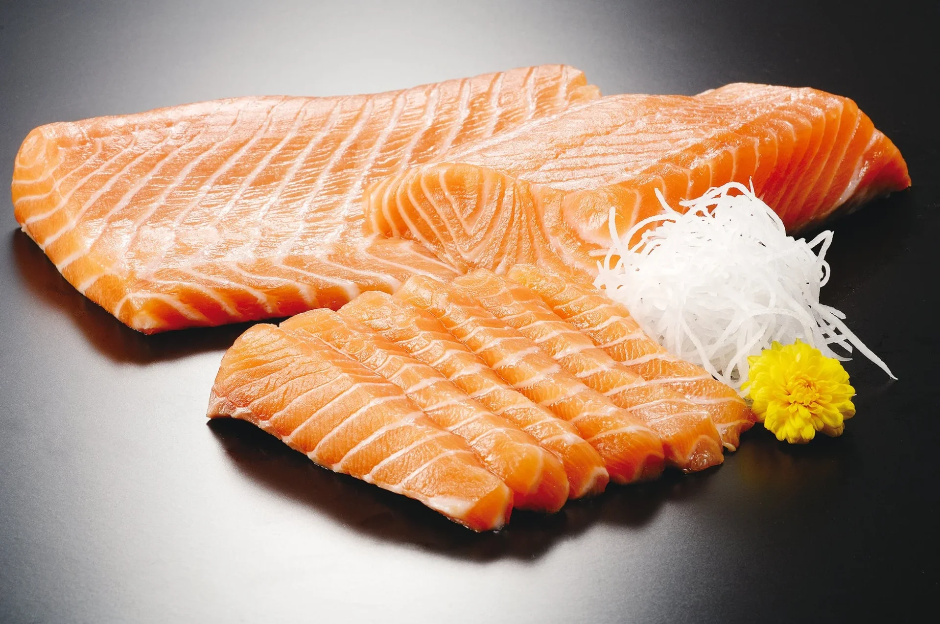 新鮮な生アトランティックサーモンの刺身が、大根のツマと菊の花と共に盛り付けられている。