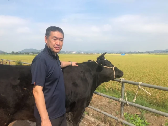 近江屋牛肉店三代目店主の寺出昌弘氏が牛とともに写る牧場での写真