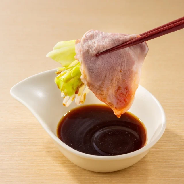 ラム肉を巻いた野菜をジンギスカンだれにつける様子