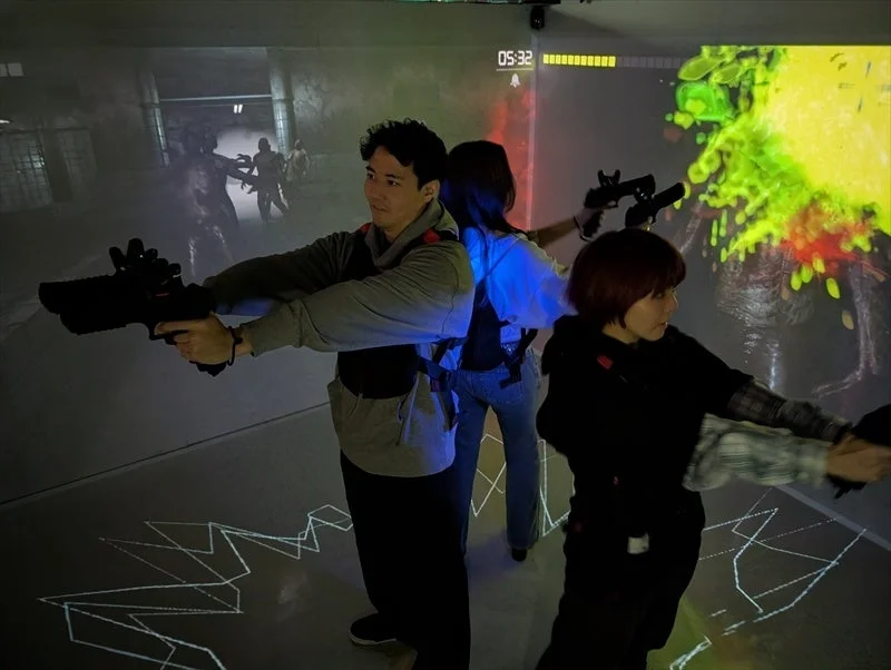 没入型アトラクション「CUBE」で銃を構えゾンビと戦うプレイヤーたち。