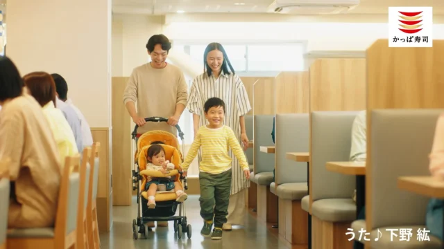 ベビーカーと子供連れの家族が店舗に入るCMシーン。