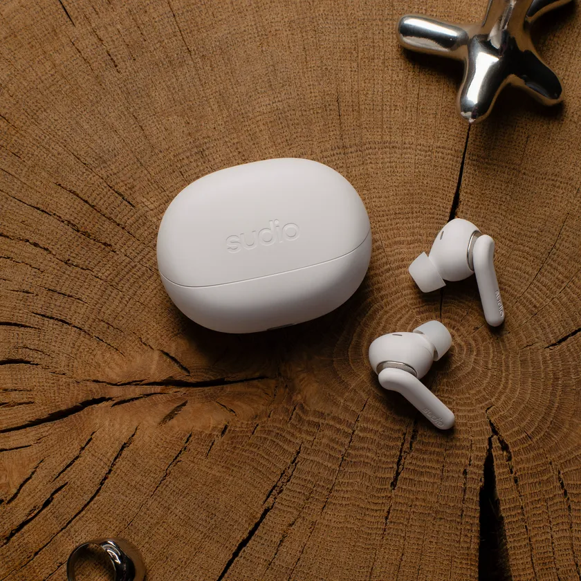 Sudio E4 Pro クラウディホワイトの充電ケースとイヤホンが木目調の背景に置かれた様子