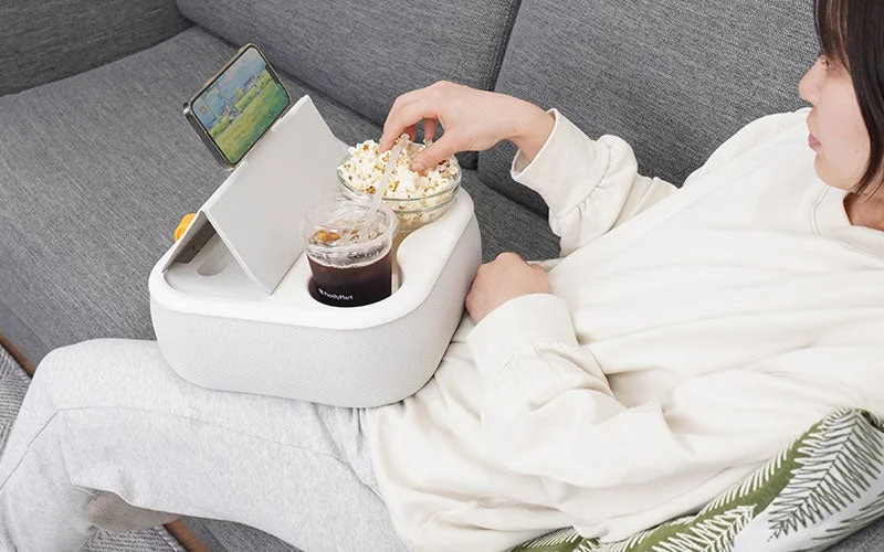 ソファで膝上テーブルクッションを使用し、ポップコーンを食べる女性